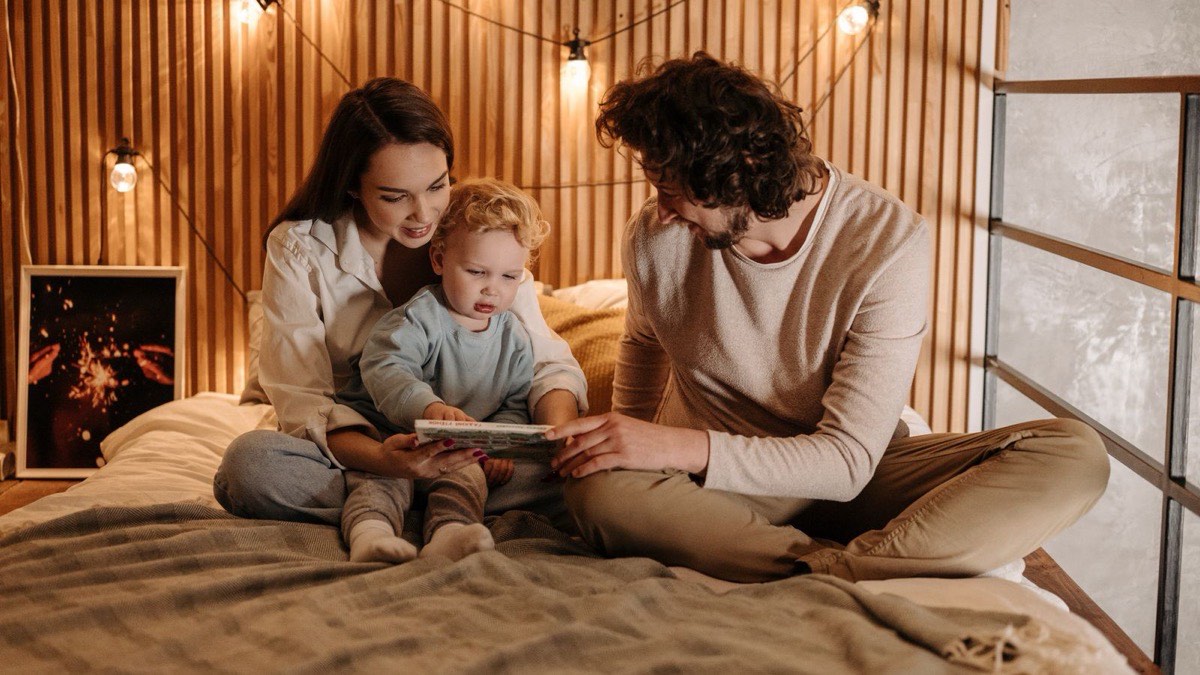 Two parents reading a bedtime story to a toddler on a bed