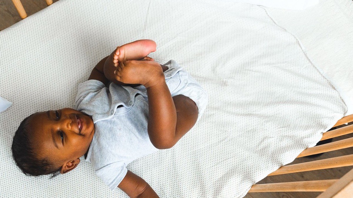 A baby lying on their back in a crib, awake, in soft daylight