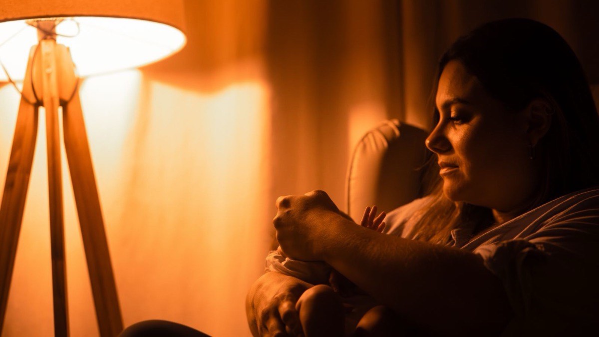 A parent cradling a baby under warm lamplight at night