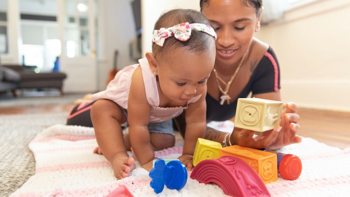 A parent and baby playing with blocks on a rug
