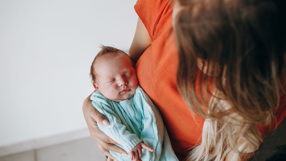 A newborn asleep in a parent’s arms, daylight