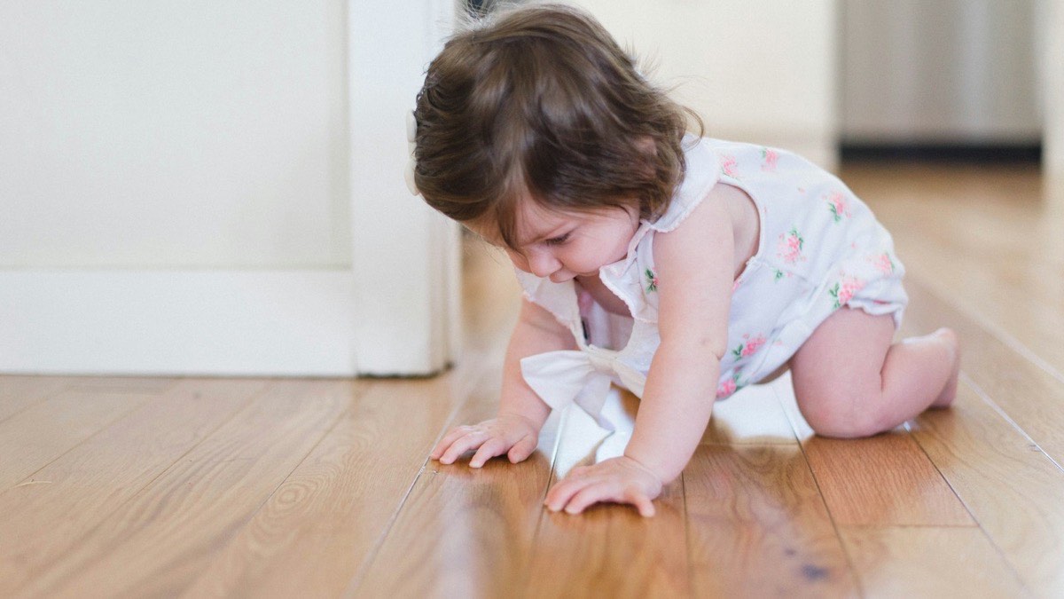 A baby crawling across a wooden floor at home